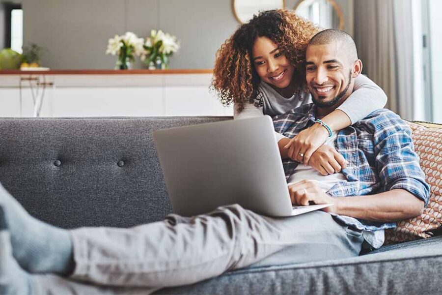 Young couple in their 30s looking at a laptop while relaxing on a couch
