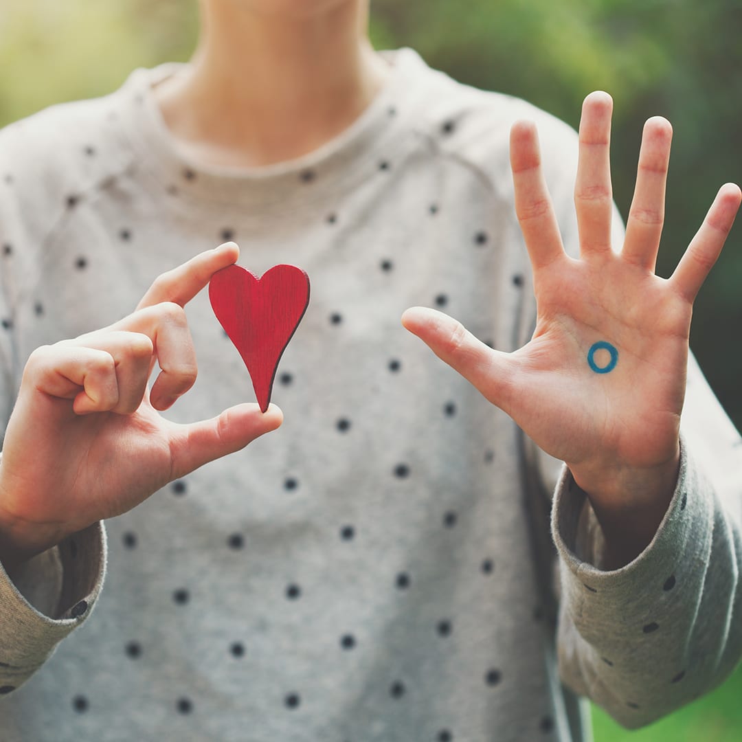 girl holding a heart shape on right hand and showing the blue circle with palm open on the left hand