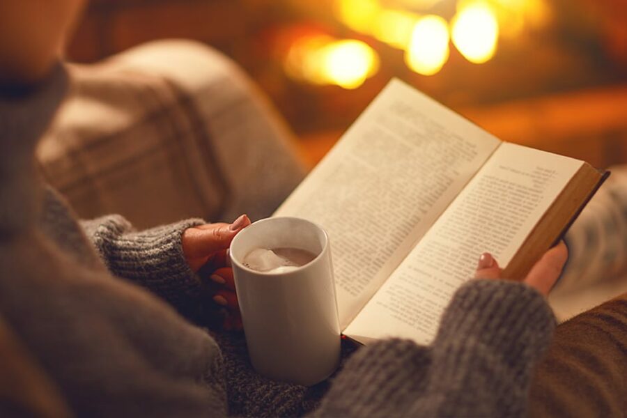 woman reading a book with a hot coco on a warm cozy environment