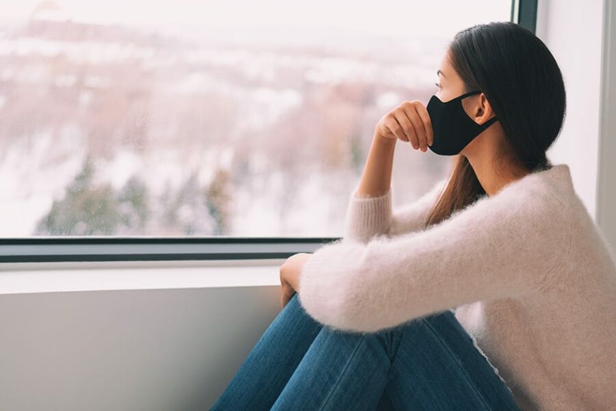 woman with face mask looking outside the window on winter