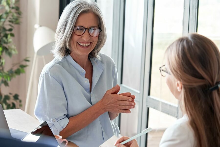 Happy mature old female mentor coach laughing training young interns at group office meeting professional workshop. Cheerful middle aged teacher professor talking to students at university