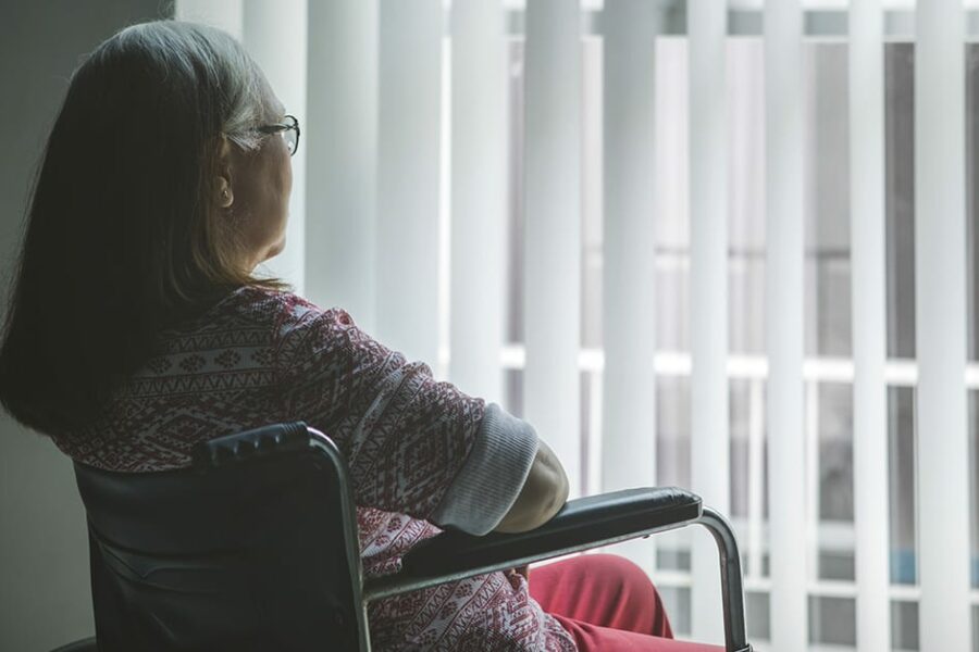Old woman with stroke on a wheelchair looking out the window