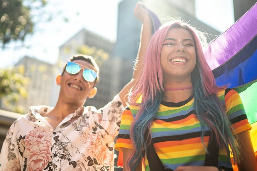 a woman in rainbow shirt and a man holding the pride flag on pride parade