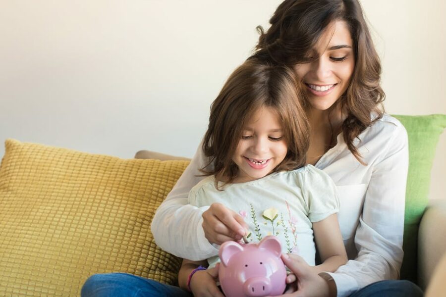 Mother and Daughter on the couch putting coin a pink piggy bank