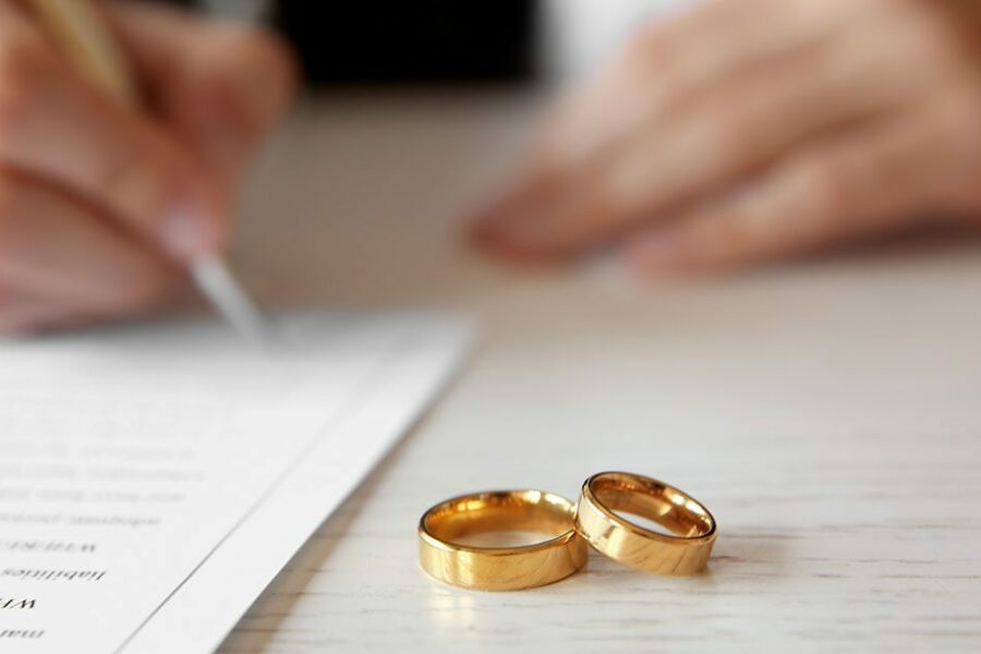 Signing a prenuptial agreement with gold wedding rings on the table