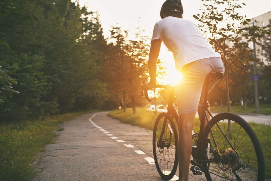 The young guy in casual clothes is cycling on the road in the evening city