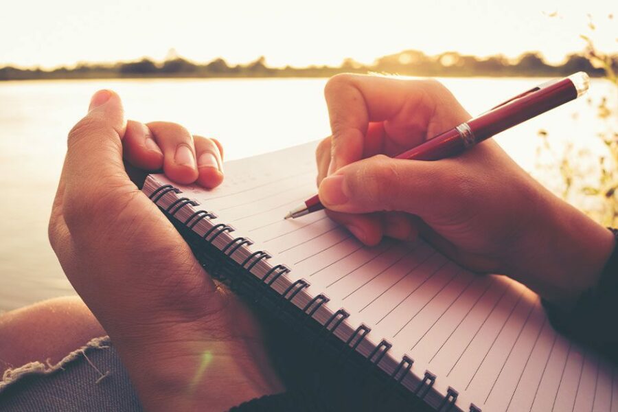 close up hand of young woman with pen writing a journal